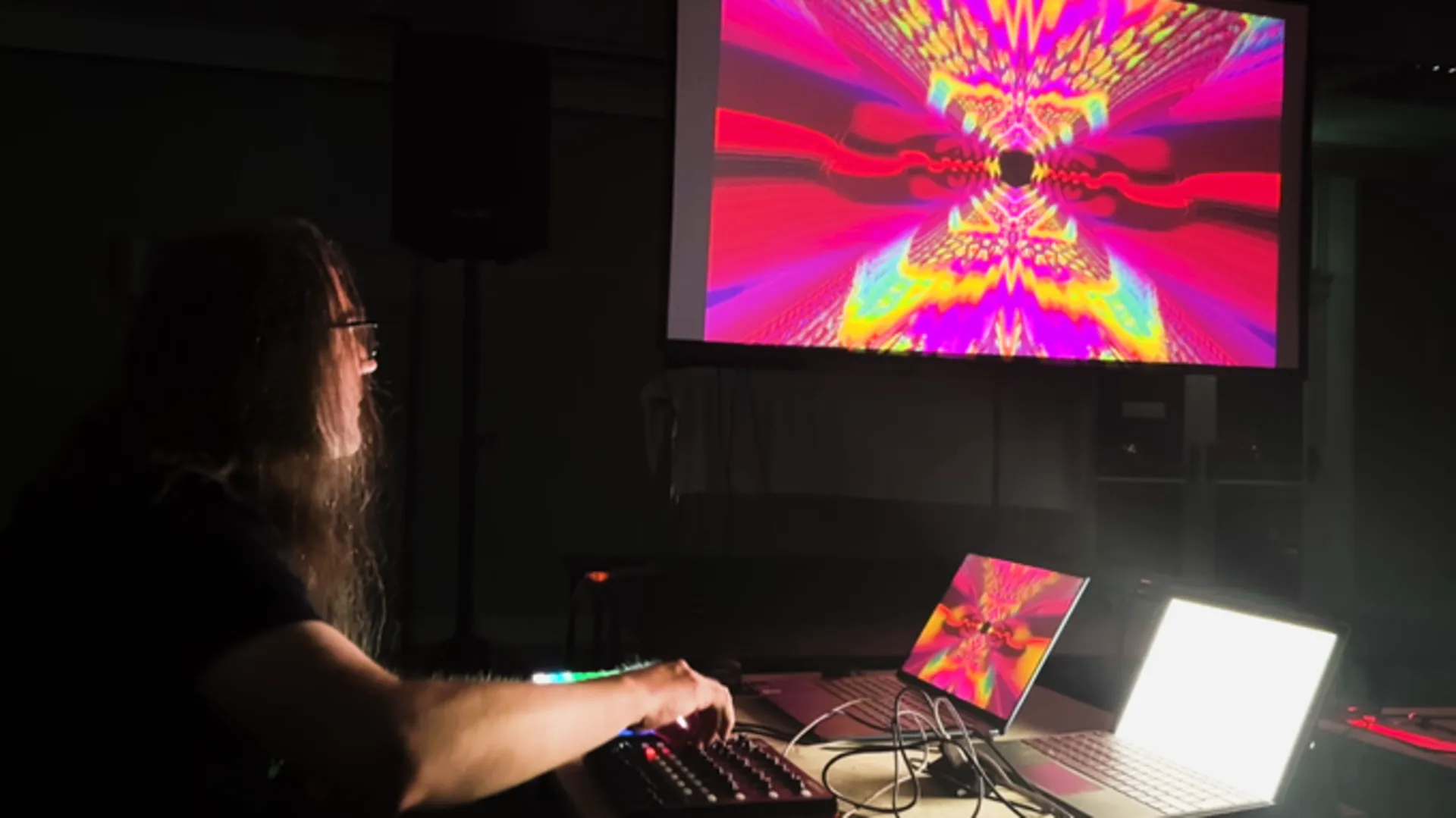 Jeff Minter at his workstation in Wales, illuminated by a large screen showing one of his psychedelic light-synth programs.