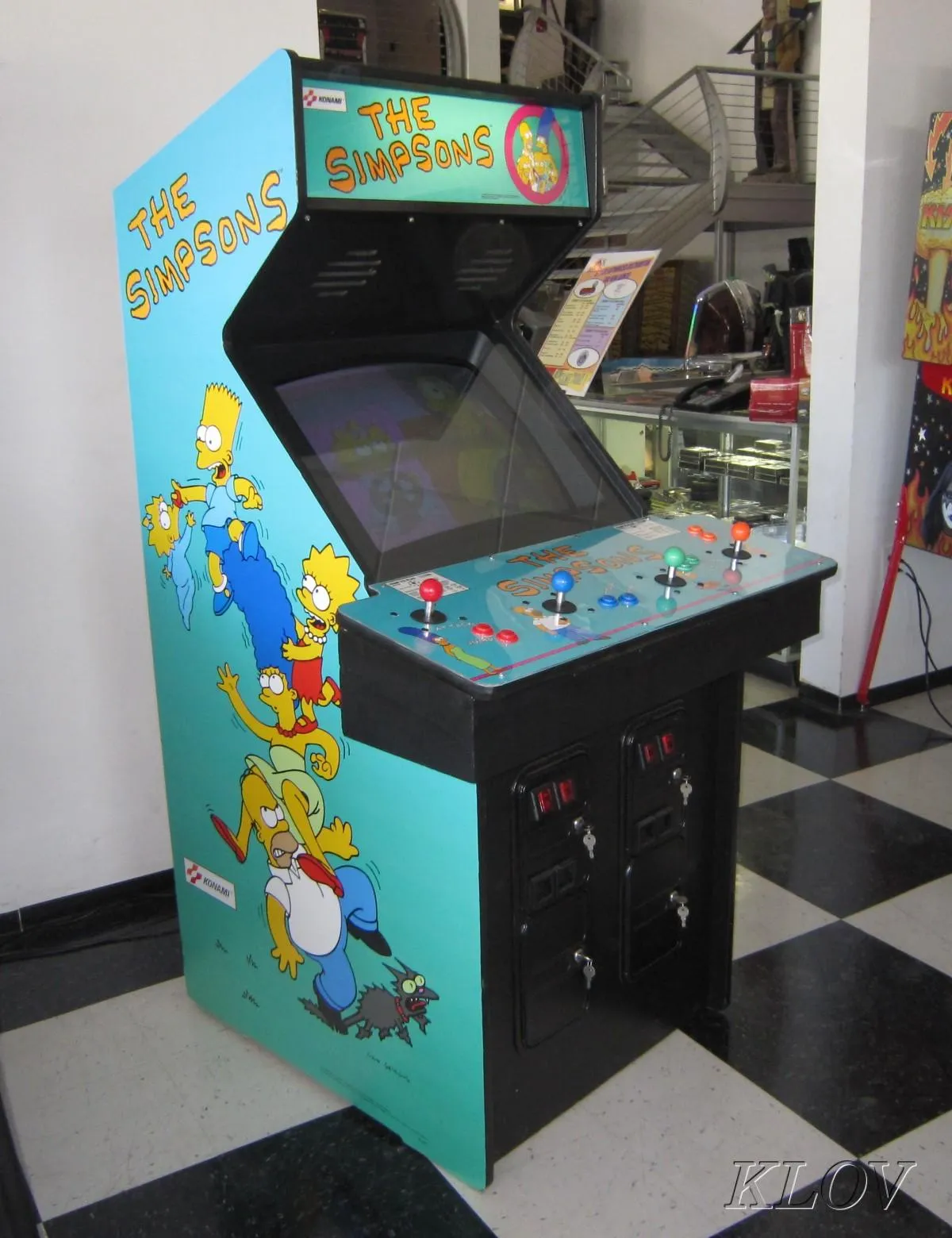 A four-player upright Konami Simpsons arcade cabinet, side art showing the family stacked one on top of another, illuminated marquee above the screen.