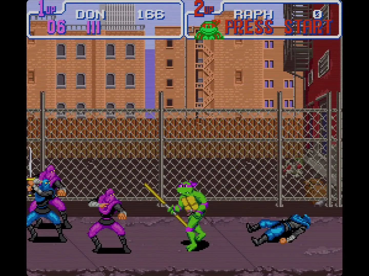 Donatello stands with his bo staff outside a chain-link fence at night, two purple Foot Soldiers preparing to attack while a third lies stunned behind him.